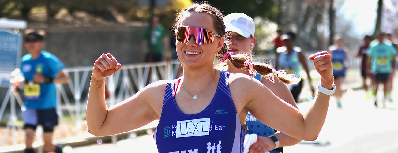 team eye and ear marathon female runner smiling with her hands in the air